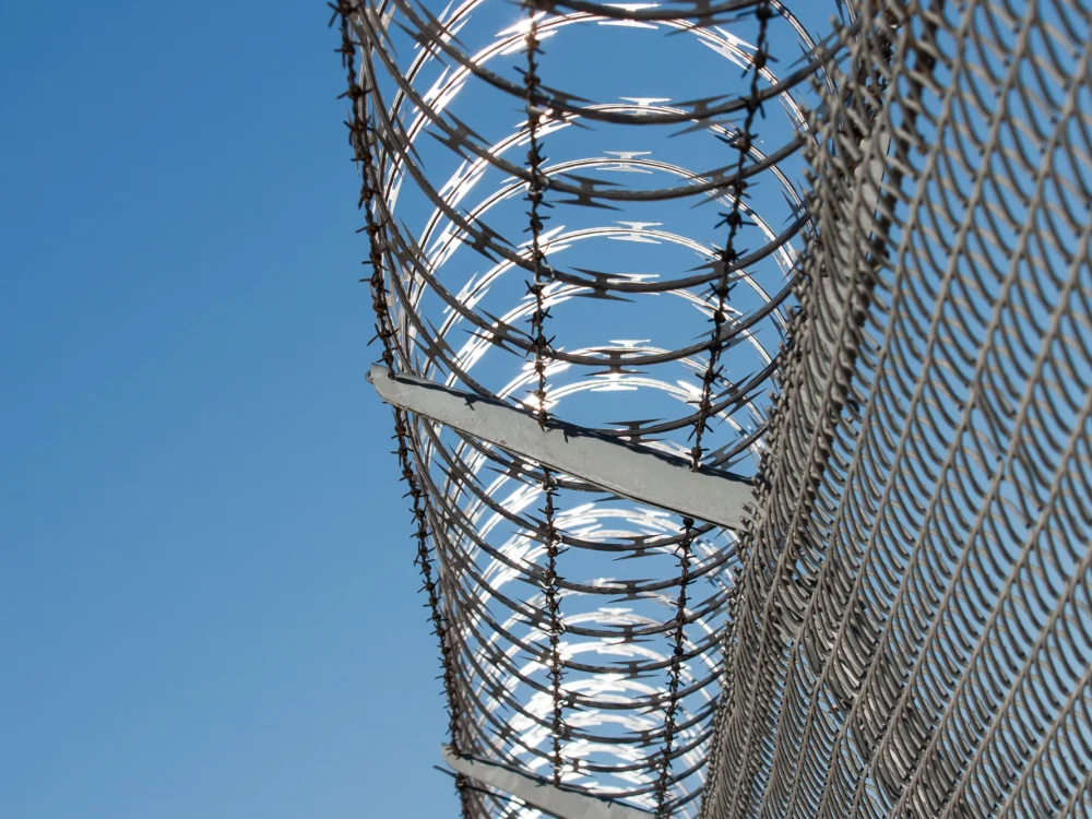 Chain-link fence topped with razor wire coils against a clear blue sky
